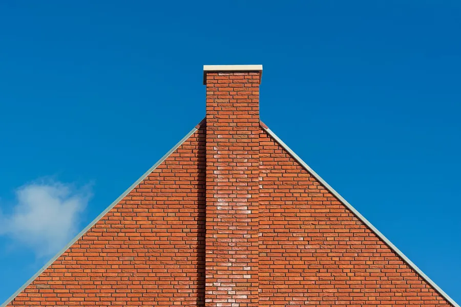 Red brick wall rising to the ridge of a pitched roof with a brick chimney on the wall line