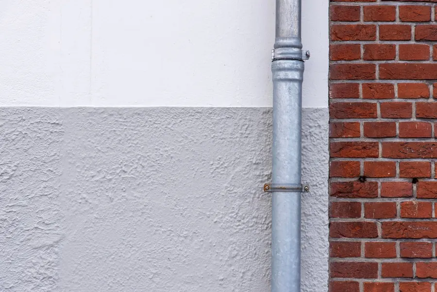 Cast iron downpipe with a socketed joint running down a brick and rendered wall