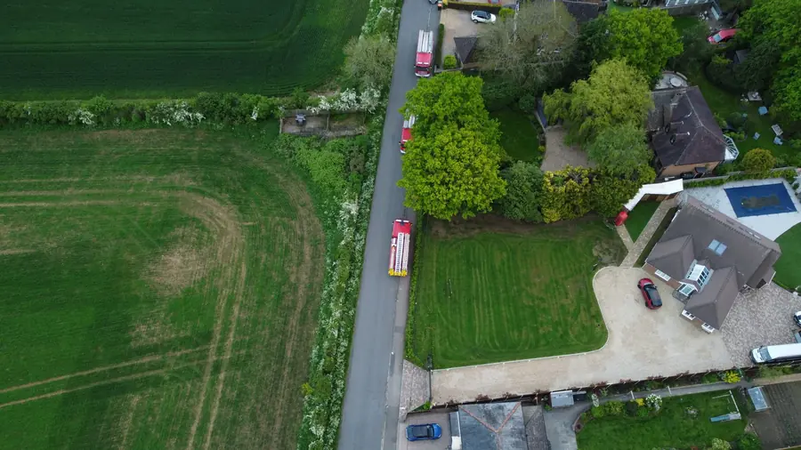 Aerial view of a chalet bungalow with roof windows and a gravel drive on a wide plot backing onto farmland