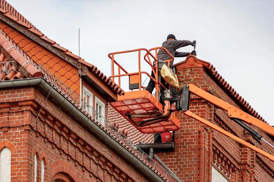 A worker using a cherry picker access platform to reach roof level