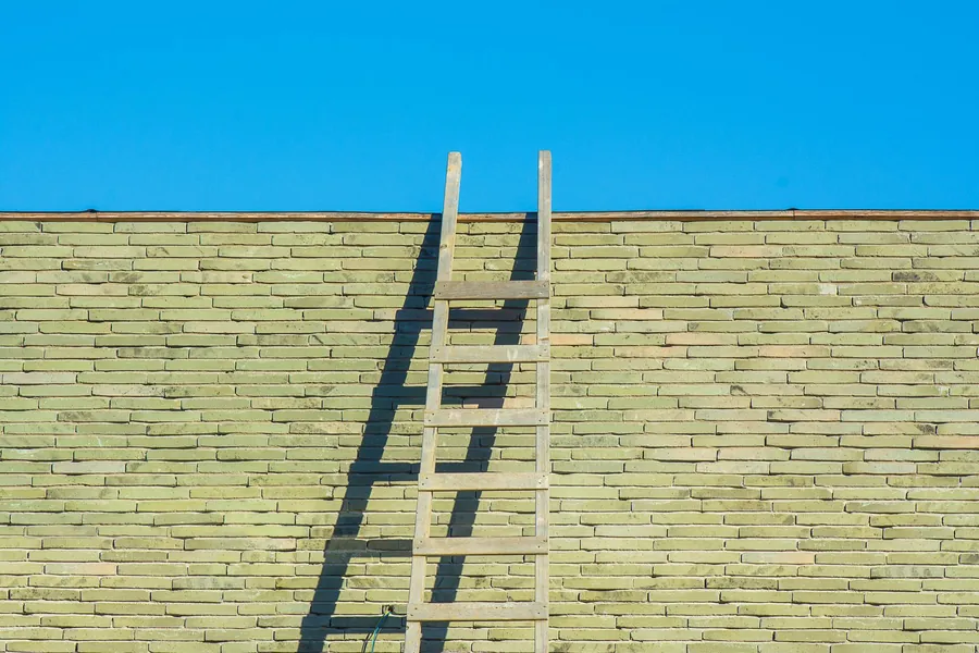 A ladder left leaning against a brick wall while a Croydon roof repair waits to be completed