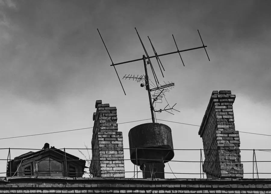 Two weathered brick chimney stacks with eroded joints and an old TV aerial between them under a grey sky