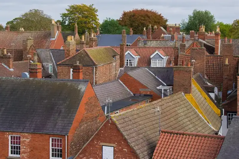 Mixed red brick and tiled rooftops with chimneys and patched slopes in an English town