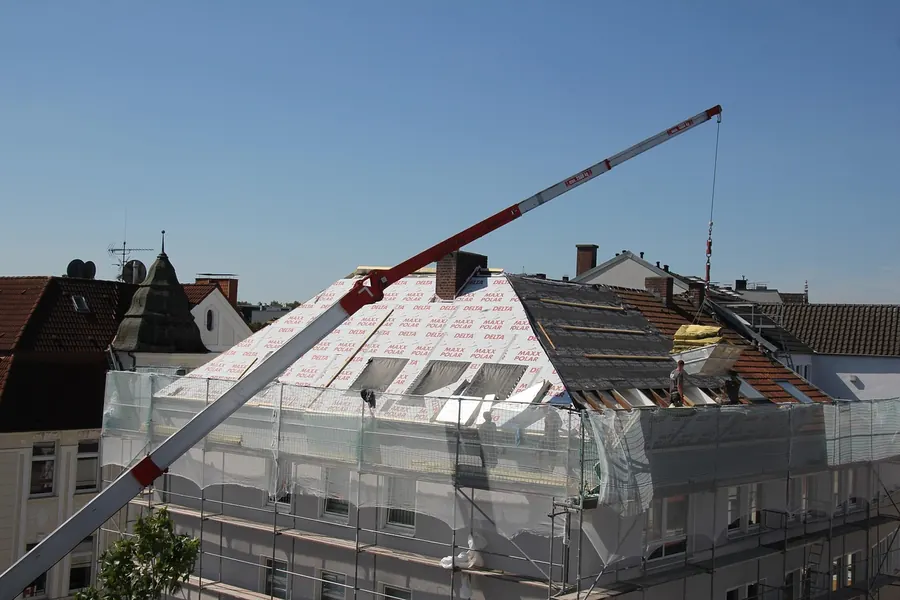 House roof stripped and covered in pale breathable membrane, wrapped in scaffolding with a crane overhead