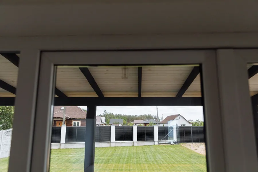 View from inside a single-storey extension through its frame towards a lawned back garden and fence