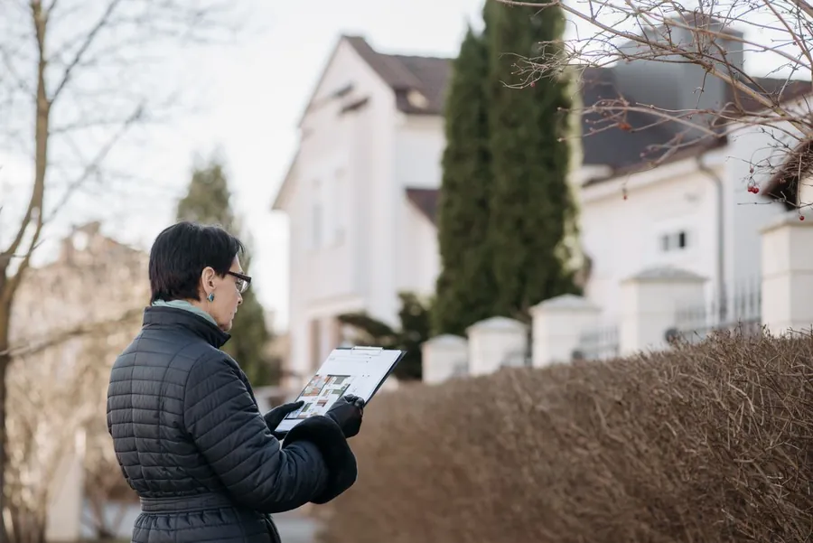 A surveyor with a clipboard inspecting the outside of a house before a sale