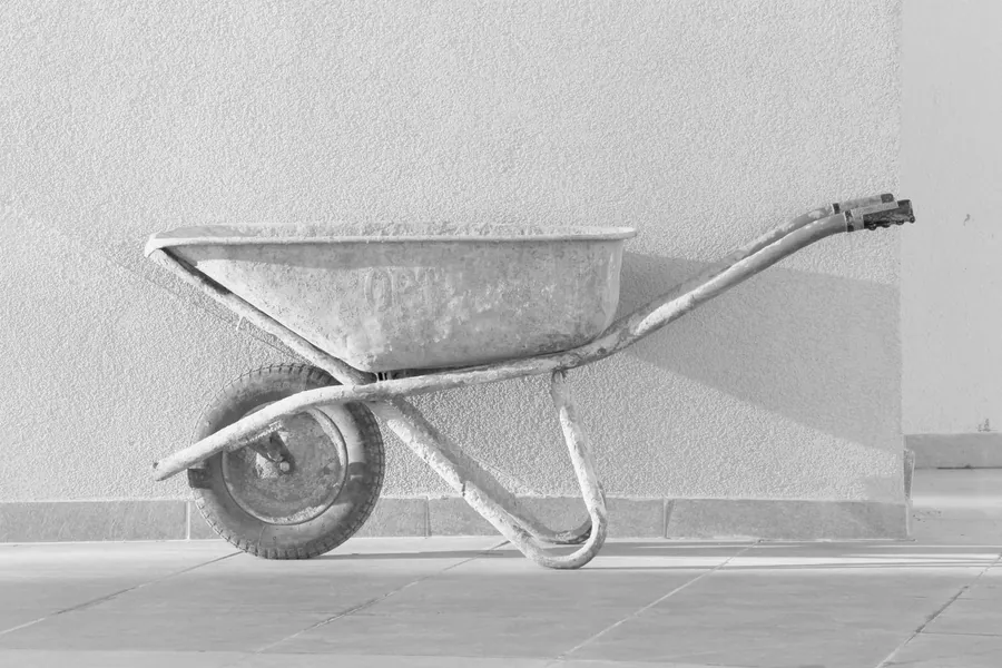 An empty builder's wheelbarrow leaning against a pale rendered wall