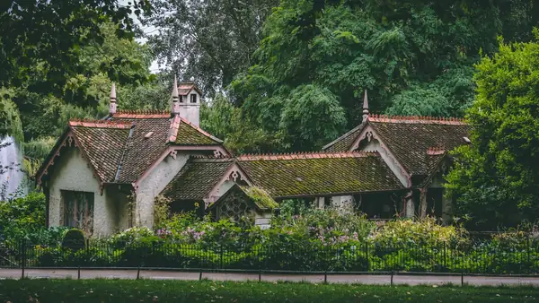 Victorian lodge-style cottage with a steep red tiled roof in a park garden